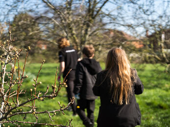 Two teenagers following an adult on a field, by small trees