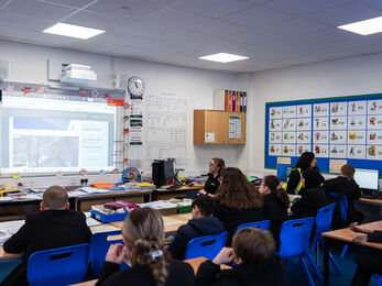 Teenagers sat in a classroom looking at an interactive whiteboard