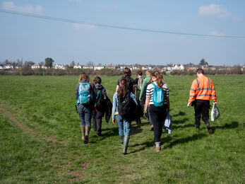 A group of young people walking away from the camera across a wide open field